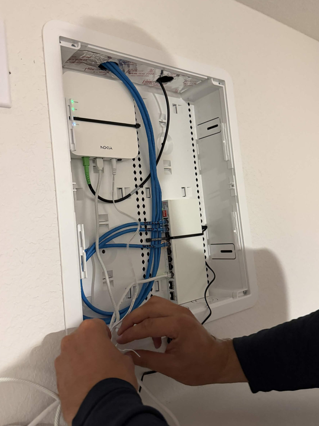 Hands connecting blue Ethernet cables in a home network panel